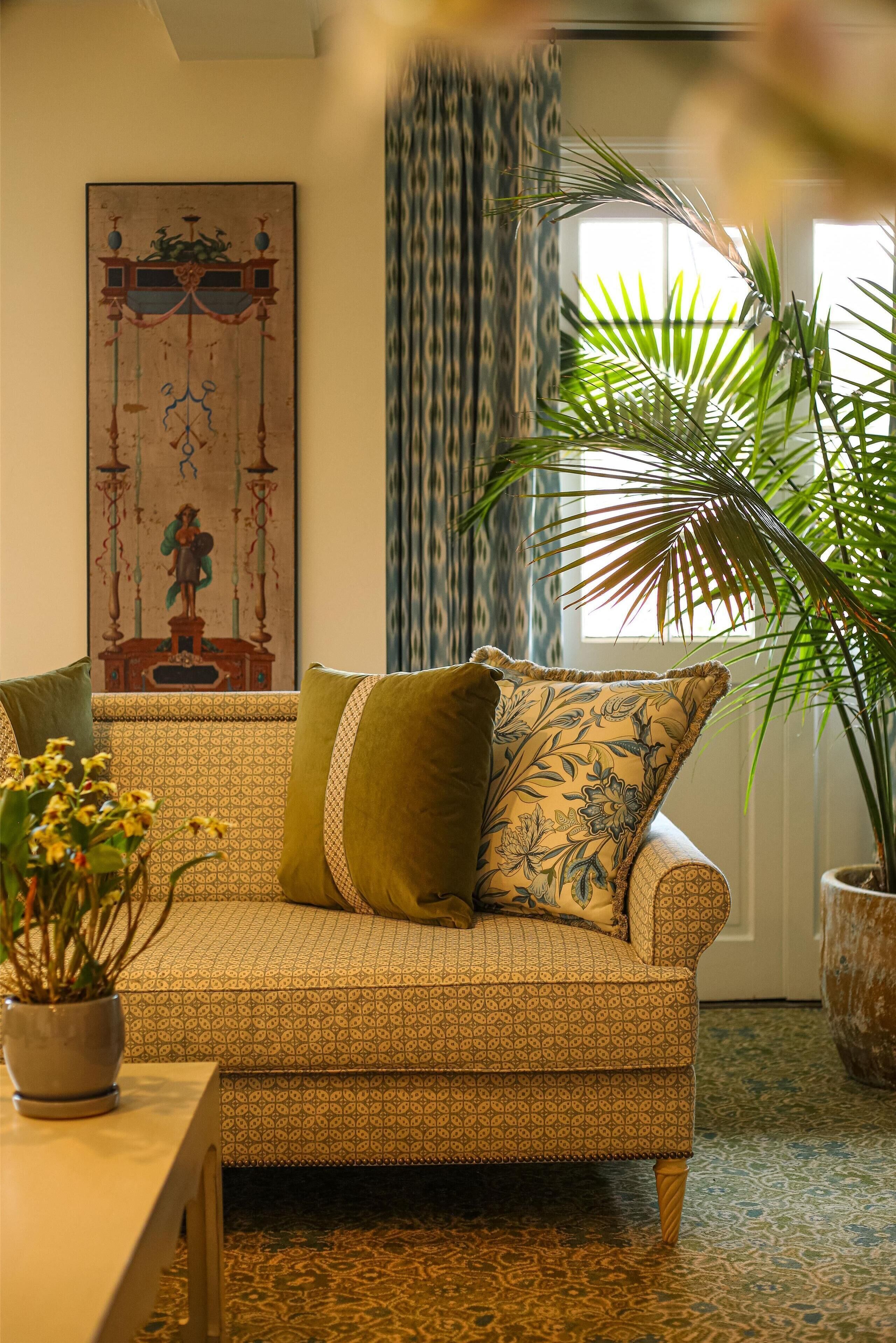 A patterned sofa with a decorative pillow, a potted plant, and a framed artwork on the wall.