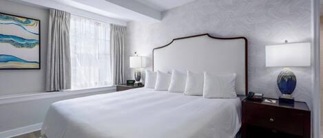 A hotel room with a large bed, a nightstand with a lamp, a painting on the wall, and a window with curtains.