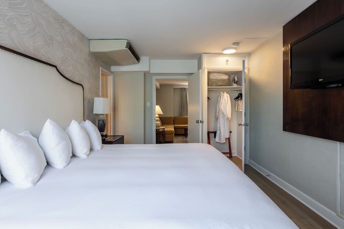 A hotel room with a large bed, a TV, a wardrobe, and a bathroom visible through an open door.