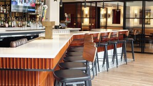 A bar area with stools, a counter, and a television screen displaying people. - The Georgetown Inn (Washington)