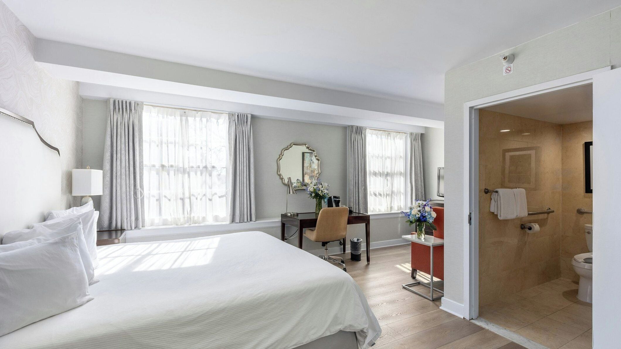 A hotel room with a bed, desk, chair, and a bathroom with a shower and toilet.