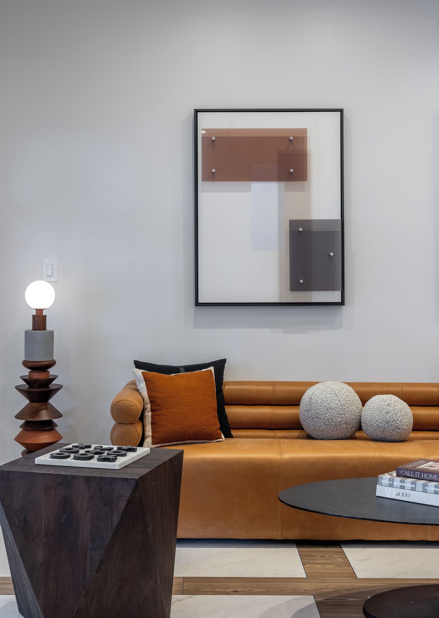 A modern living room with a brown leather sofa, a round coffee table, and a minimalist wall art piece.