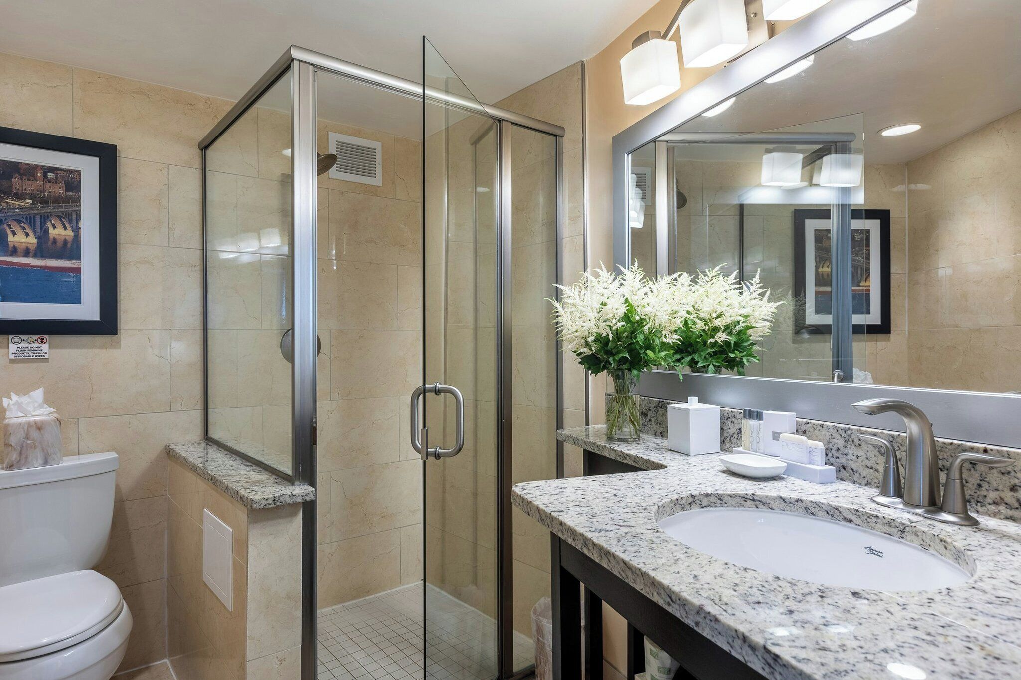 A modern bathroom with a glass-enclosed shower, a sink with a marble countertop, and a large mirror.