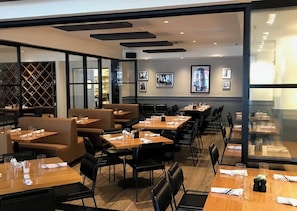 A restaurant with booths and tables, framed pictures on the wall, and a wine rack in the background.