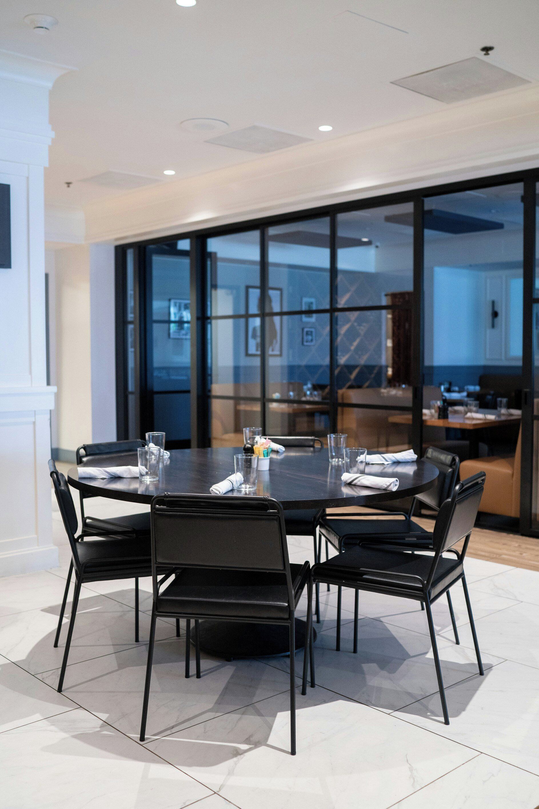 A conference room with a round table, black chairs, and a glass partition.
