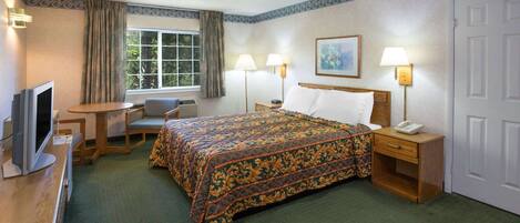 Une chambre d’hôtel comprenant un lit, un bureau avec une télévision, une chaise, une fenêtre avec des rideaux et deux lampes de chevet.