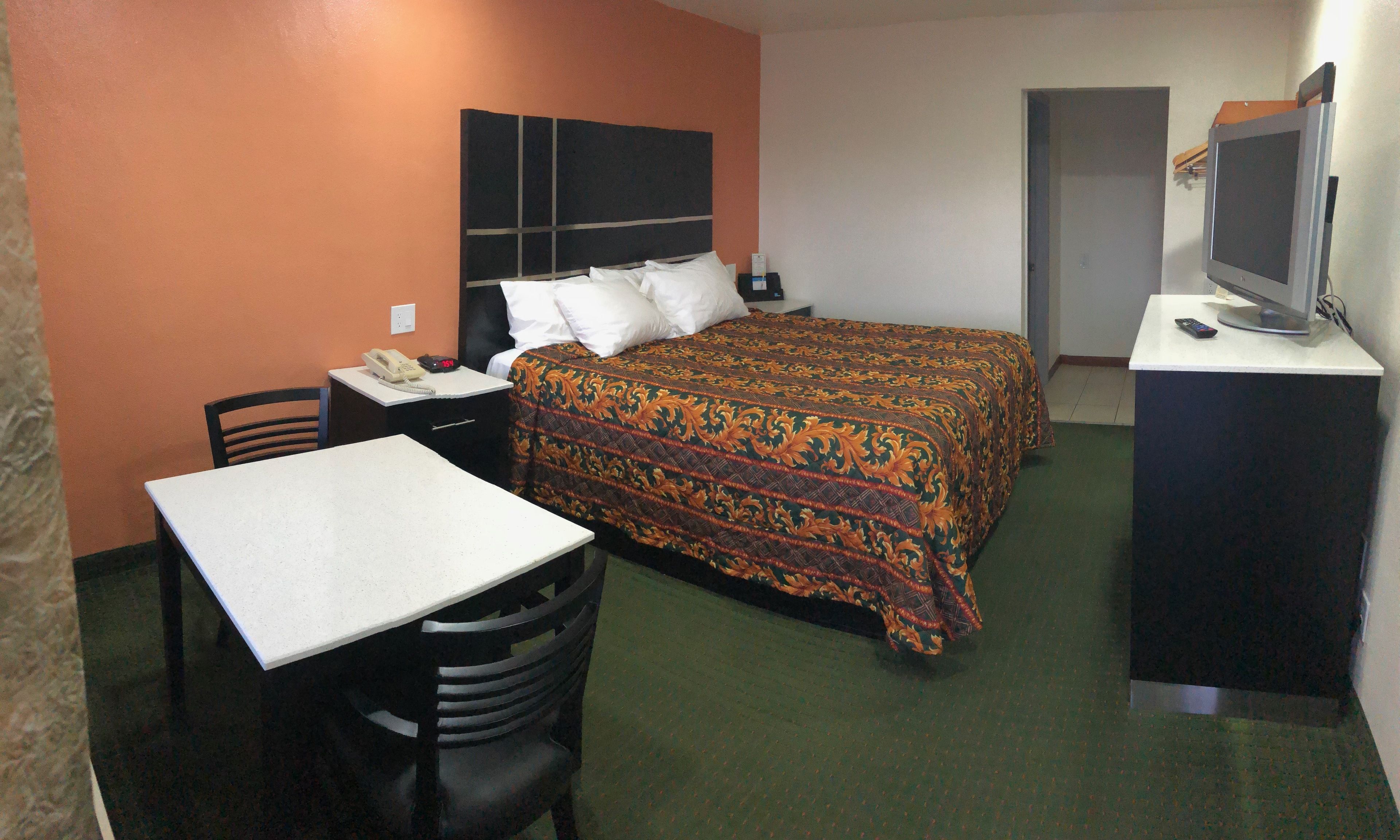 Een hotelkamer met een bed, een bureau met stoel, een televisie op een standaard en een deur.