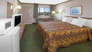 Quarto de hotel com cama, televisão, secretária com cadeira, janela com cortinas e um quadro na parede.