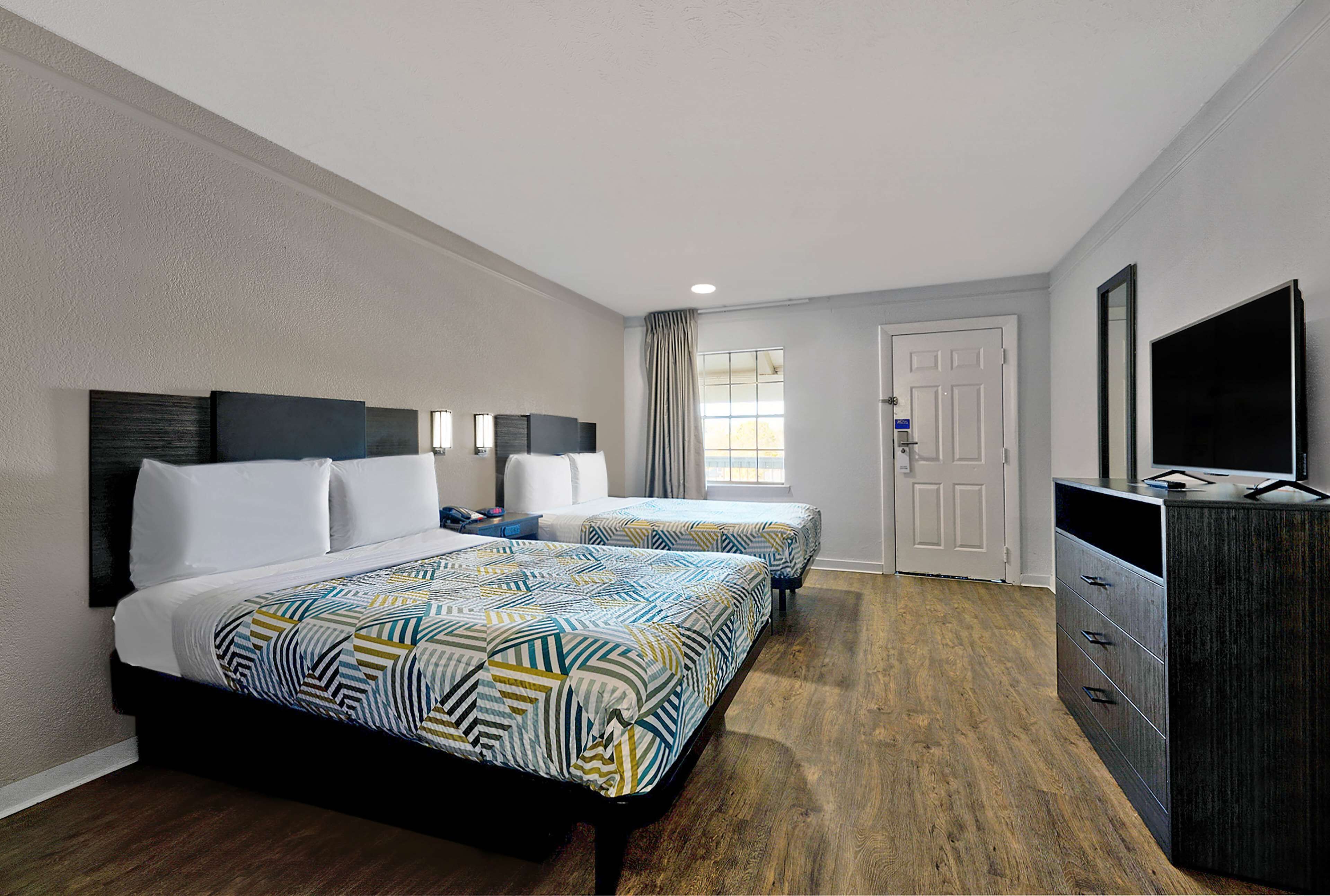 A hotel room with two beds, a dresser, a TV, and a window with curtains.