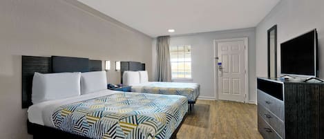 A hotel room with two beds, a dresser, a TV, and a window with curtains.