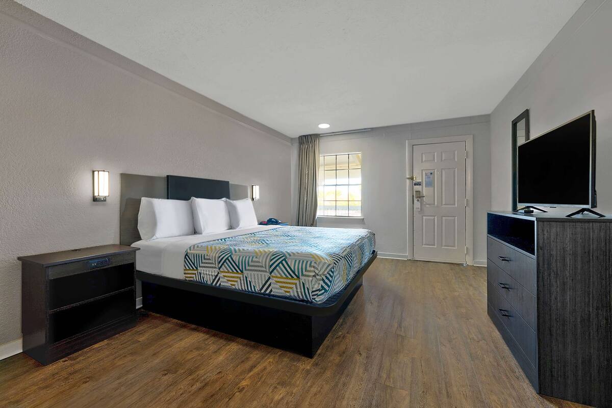 Une chambre d’hôtel moderne équipée d’un lit, d’une table de chevet, d’une commode et d’un téléviseur.
