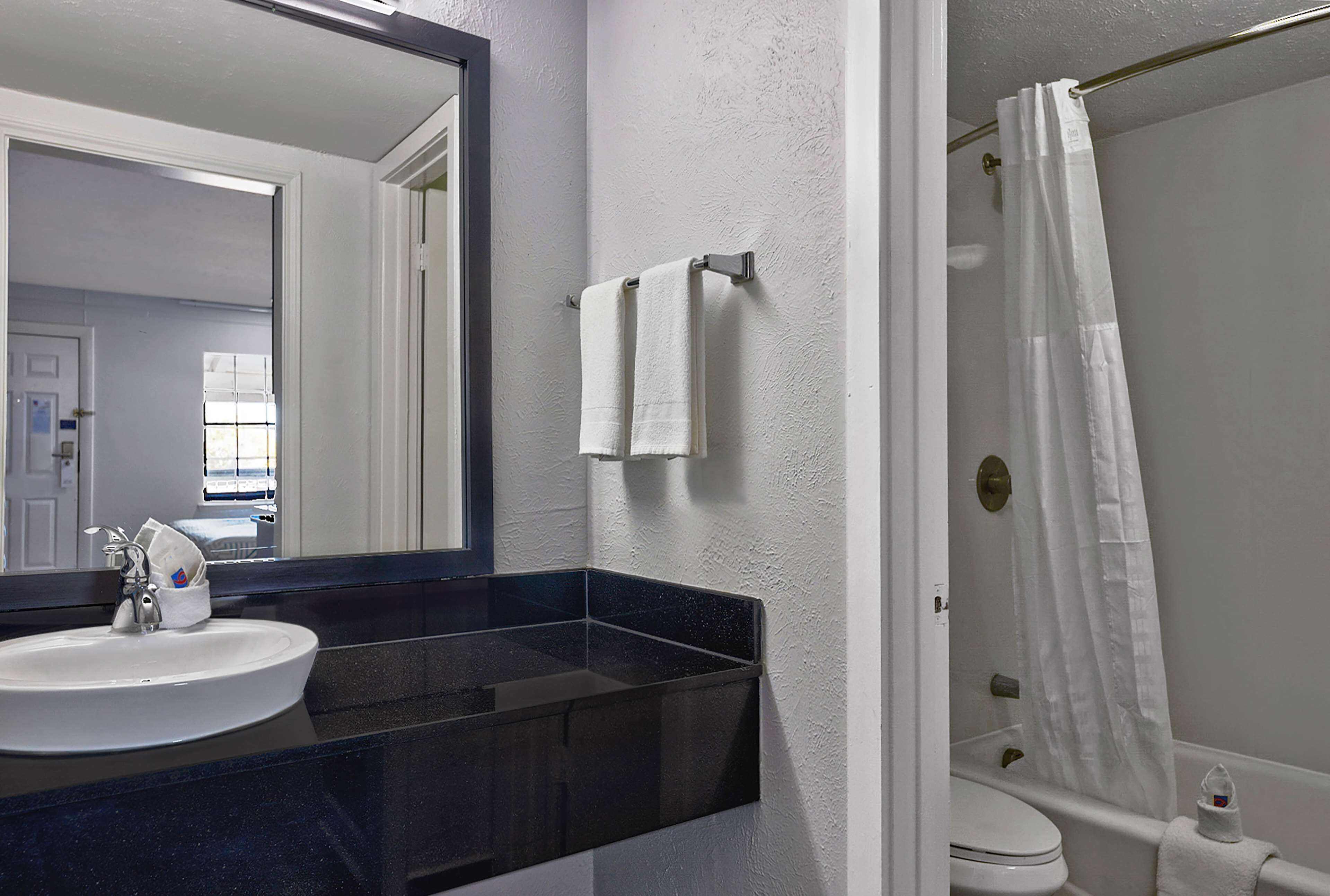 A bathroom with a white sink, a mirror, a black countertop, a white towel, and a shower curtain.