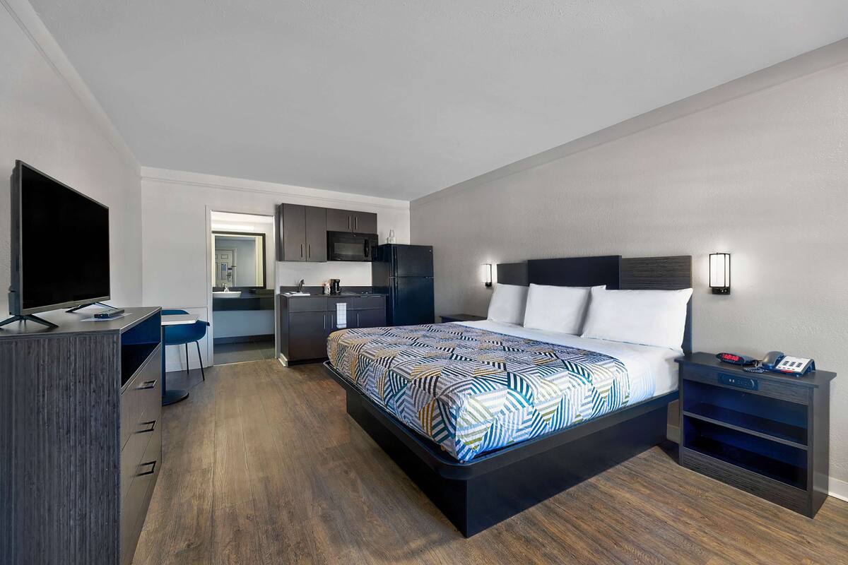 Une chambre d’hôtel moderne équipée d’un grand lit, d’un bureau, d’une télévision à écran plat, d’un four à micro-ondes et d’une petite kitchenette.