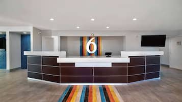 A modern reception desk with a large number '6' above it, a flat-screen TV mounted on the wall, and a colorful striped carpet in front.