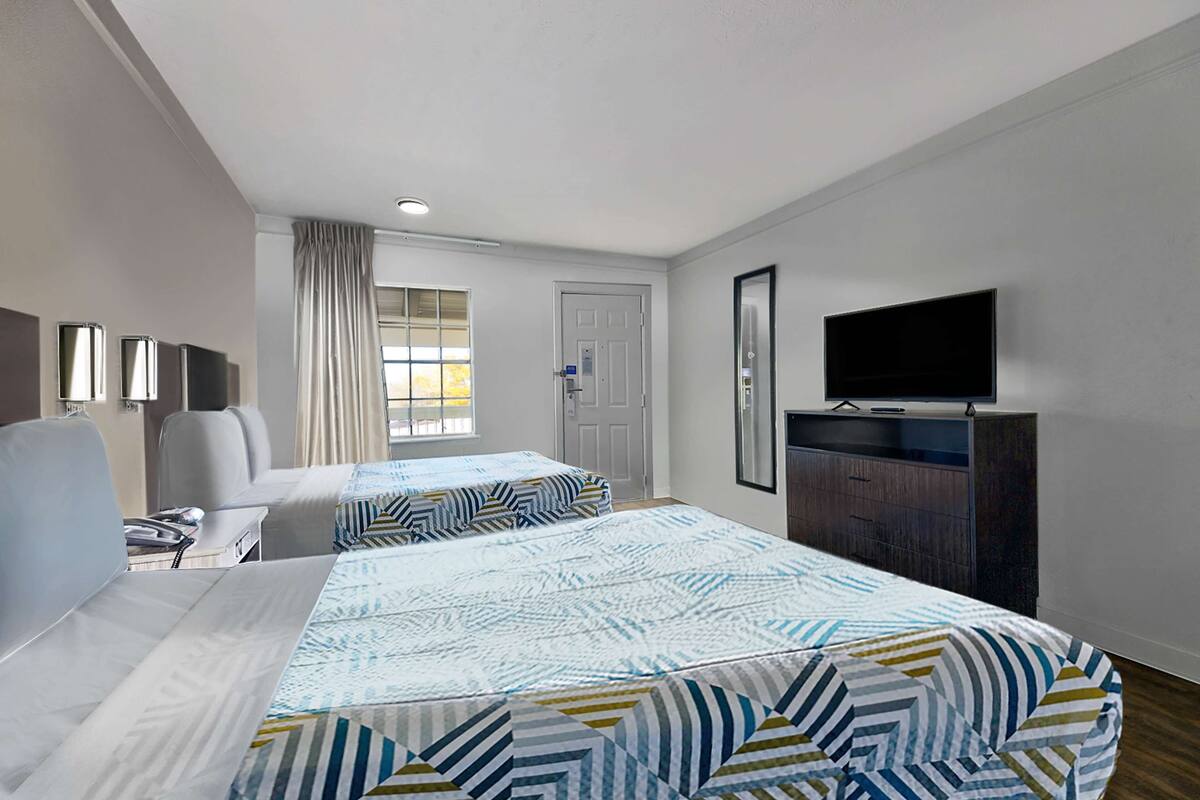 Une chambre d’hôtel avec deux lits, une télévision, un bureau et une fenêtre avec des rideaux.