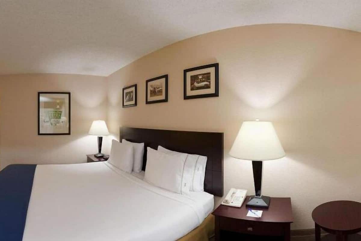 A hotel room with a large bed, two bedside tables with lamps, a small round table, and three framed pictures on the wall.