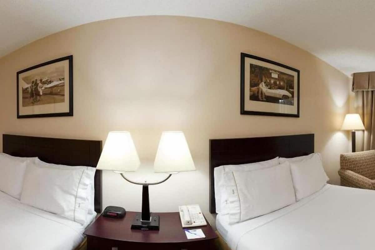 A hotel room with two beds, a nightstand with a lamp, and two framed pictures on the wall.