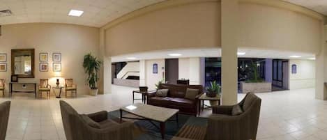A spacious lobby with a curved ceiling, a central seating area with sofas and a coffee table, and a large potted plant.