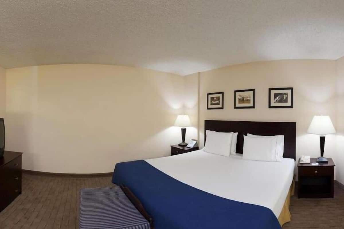 A hotel room with a large bed, two bedside tables with lamps, a television, and three framed pictures on the wall.