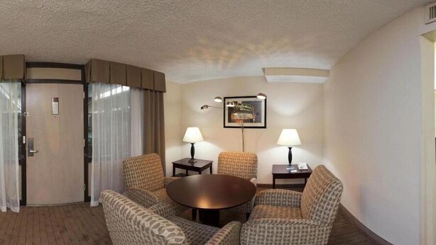 A hotel room with a round table, two armchairs, a sofa, a door, and a framed picture on the wall. - Holiday Inn Express Little Rock Airport by IHG (Little Rock)
