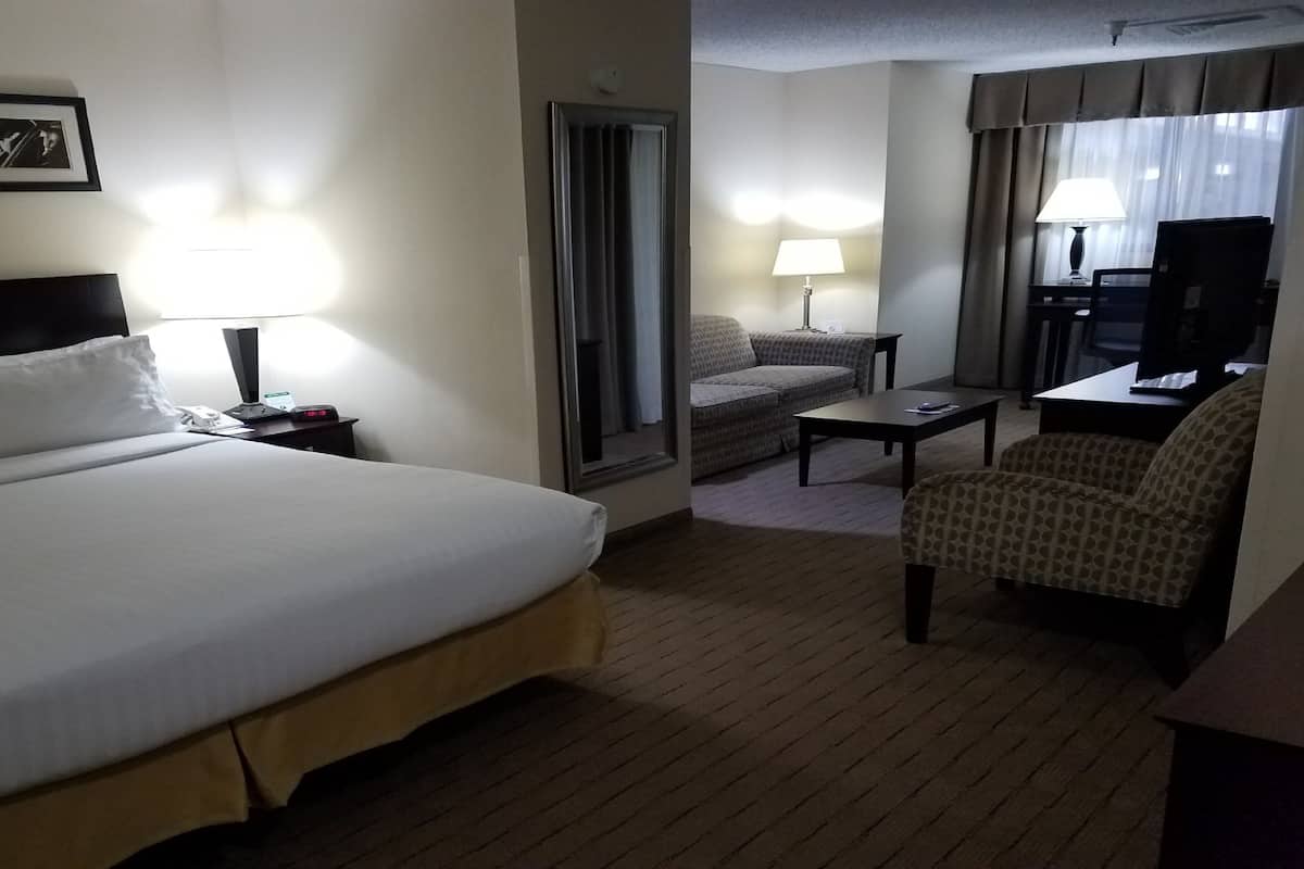 A hotel room with a large bed, a desk, a chair, a sofa, and a TV.