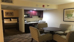 A hotel room with a bed, a kitchenette, and a dining area with patterned chairs. - Holiday Inn Express Little Rock Airport by IHG (Little Rock)