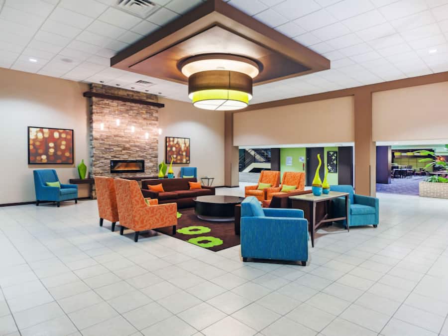 A lobby with a fireplace, seating area, and a staircase leading to an outdoor area.