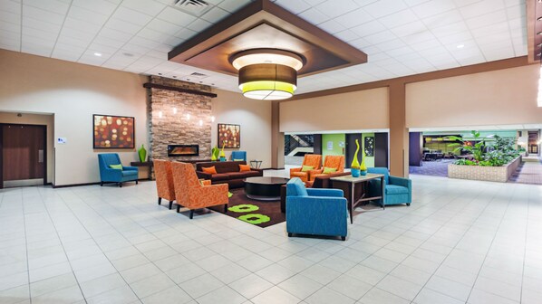 A lobby with a fireplace, seating area, and a staircase leading to an outdoor area.