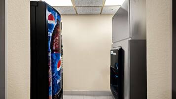 Un pasillo estrecho con un refrigerador y una máquina expendedora a la derecha, y una pared con un anuncio de Pepsi a la izquierda.