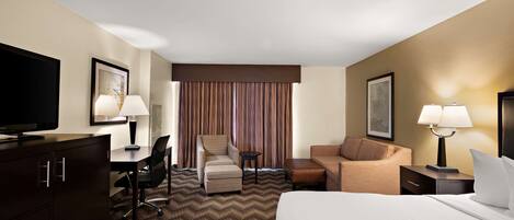 A hotel room with a bed, a desk with a chair, a sofa, a television, and a lamp.