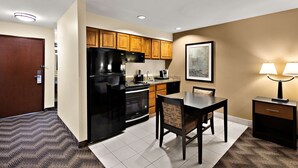 A compact kitchen with a refrigerator, stove, and microwave. There is a dining table with chairs and a small side table with a lamp. - Best Western Plus Gold Country Inn (Winnemucca)