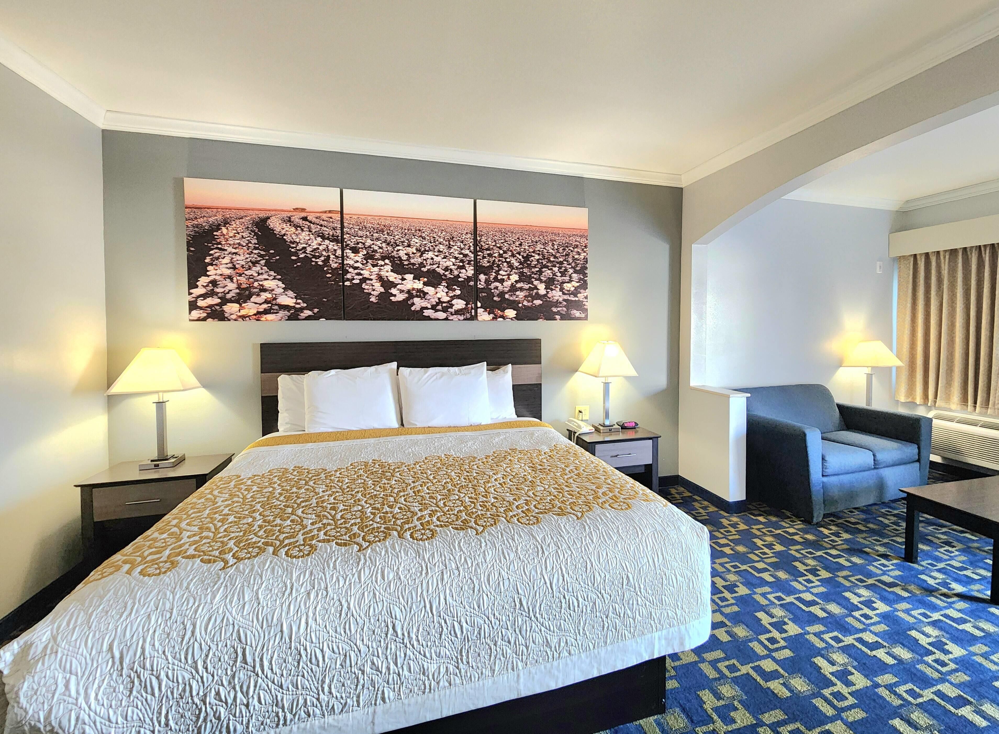 Een hotelkamer met een groot bed, twee bedlampen, een stoel, een bureau en een groot bloemig kunstwerk aan de muur.