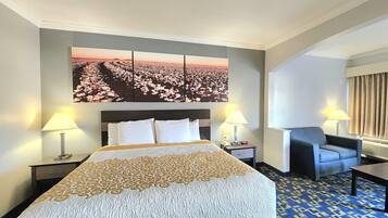 Een hotelkamer met een groot bed, twee bedlampen, een stoel, een bureau en een groot bloemig kunstwerk aan de muur.