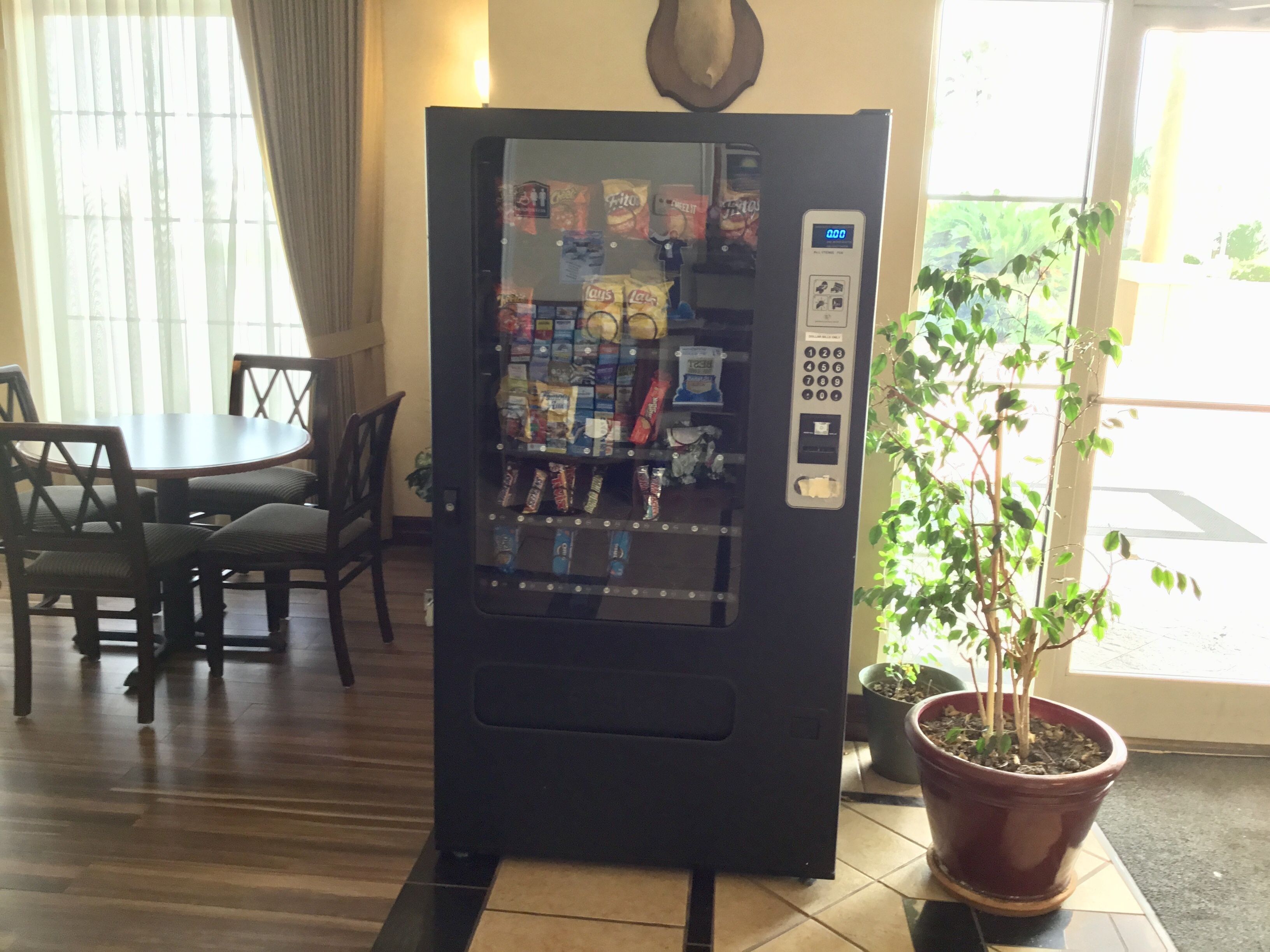 A vending machine with snacks and drinks, located in a room with a dining table and chairs.