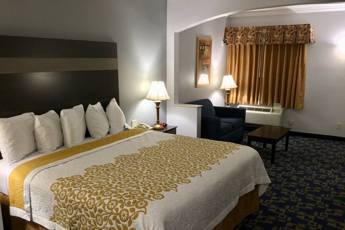 Ein Hotelzimmer mit Bett, zwei Nachttischlampen, einem Schreibtisch, einem Stuhl und einem Fenster mit Vorhängen.