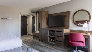 A modern hotel room with a bed, a desk with a flat-screen TV, a mirror, and a red chair. - Hampton Inn Athens (Athens)