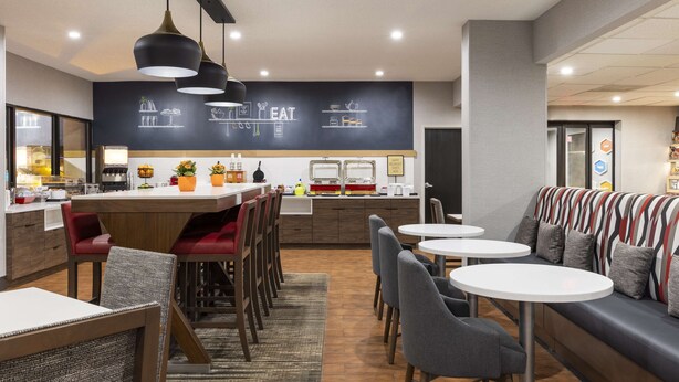 A modern cafe with a central bar, seating area, and a chalkboard menu. - Hampton Inn Athens (Athens)