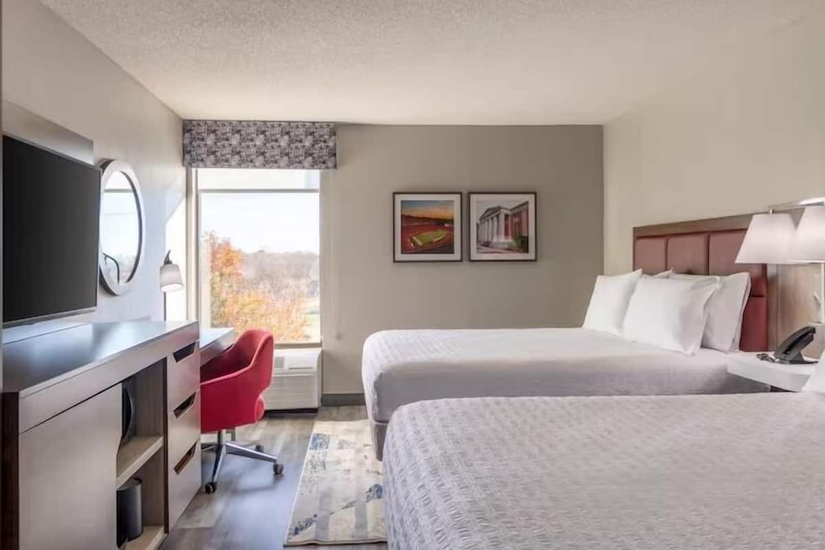 A hotel room with a bed, a desk, a TV, and two framed pictures on the wall.