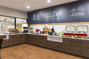A modern kitchen with wooden cabinets, a chalkboard wall with food illustrations, and various kitchen appliances.
