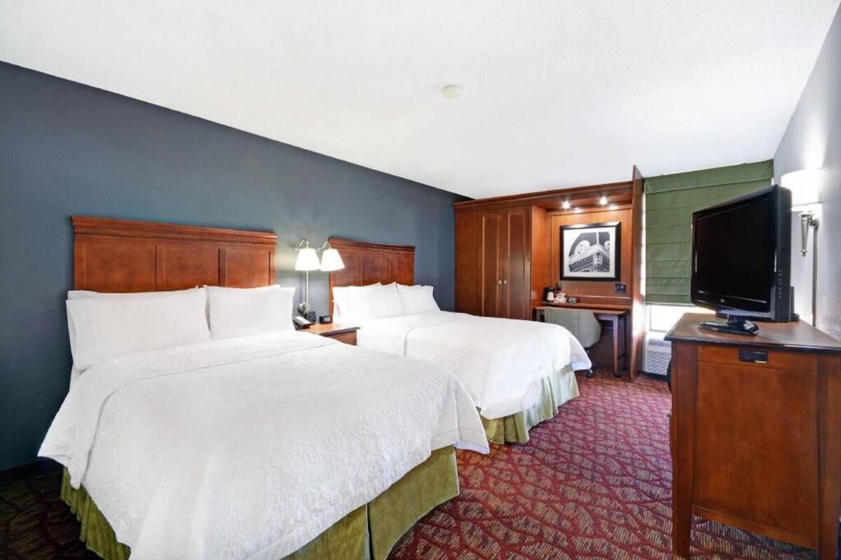 A hotel room with two beds, a desk, a television, and a framed picture on the wall.