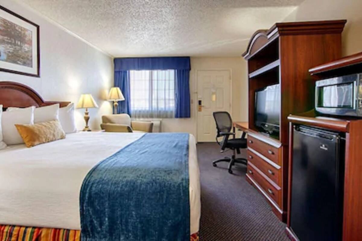 Habitación de hotel con una cama grande, un escritorio con televisor, una silla y un aparador.