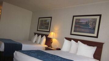 Habitación de hotel con dos camas, una mesita de noche con lámpara y dos cuadros enmarcados en la pared.