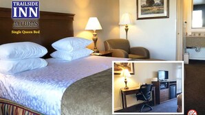 A Trailside Inn room with a single queen bed, two bedside lamps, a chair, a desk with a lamp, and a television. - Trailside Inn (Alturas)