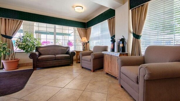 A living room with a brown sofa, a smaller armchair, a coffee table, and a potted plant. - Trailside Inn (Alturas)