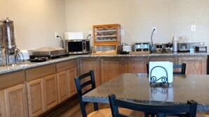 A kitchen with wooden cabinets, a granite countertop, a microwave, a coffee maker, and a small dining table with chairs. - Trailside Inn (Alturas)