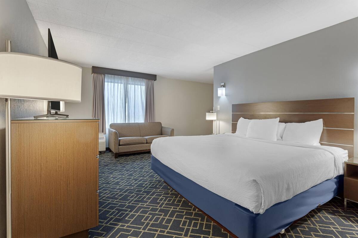 A hotel room with a large bed, a desk, a chair, and a window with curtains.