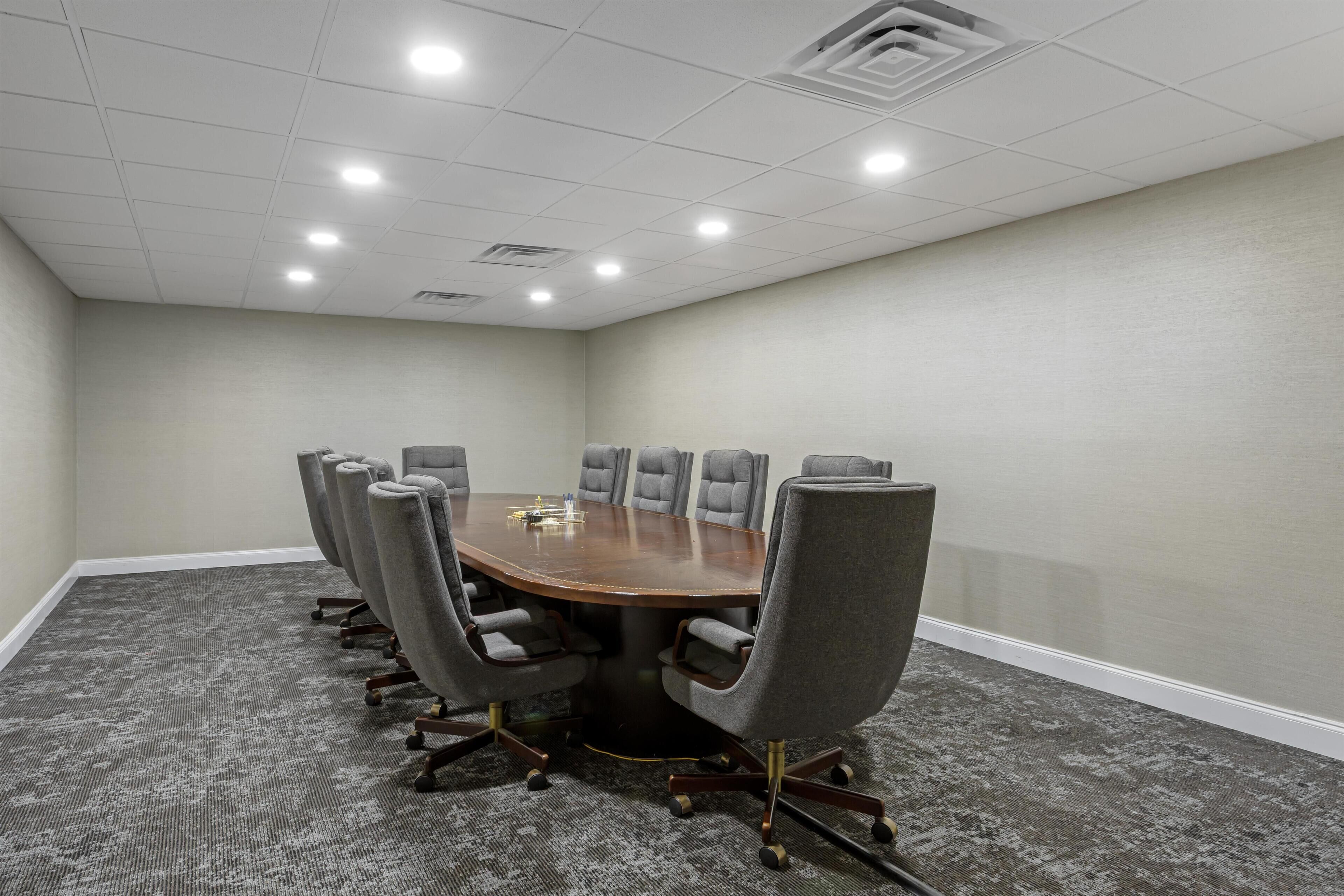 A conference room with a round table, eight gray chairs, and a carpeted floor.