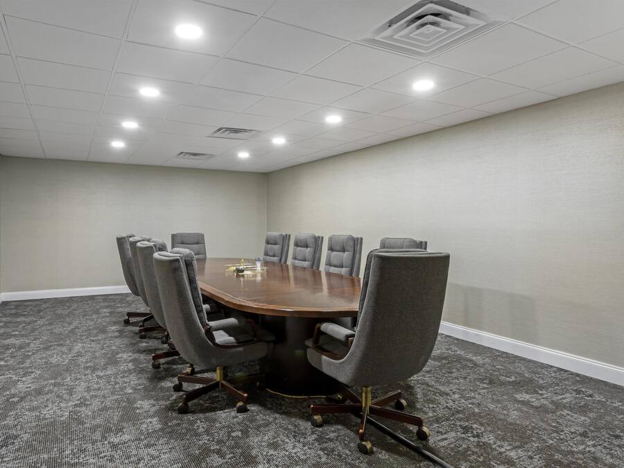 A conference room with a round table, eight gray chairs, and a carpeted floor.