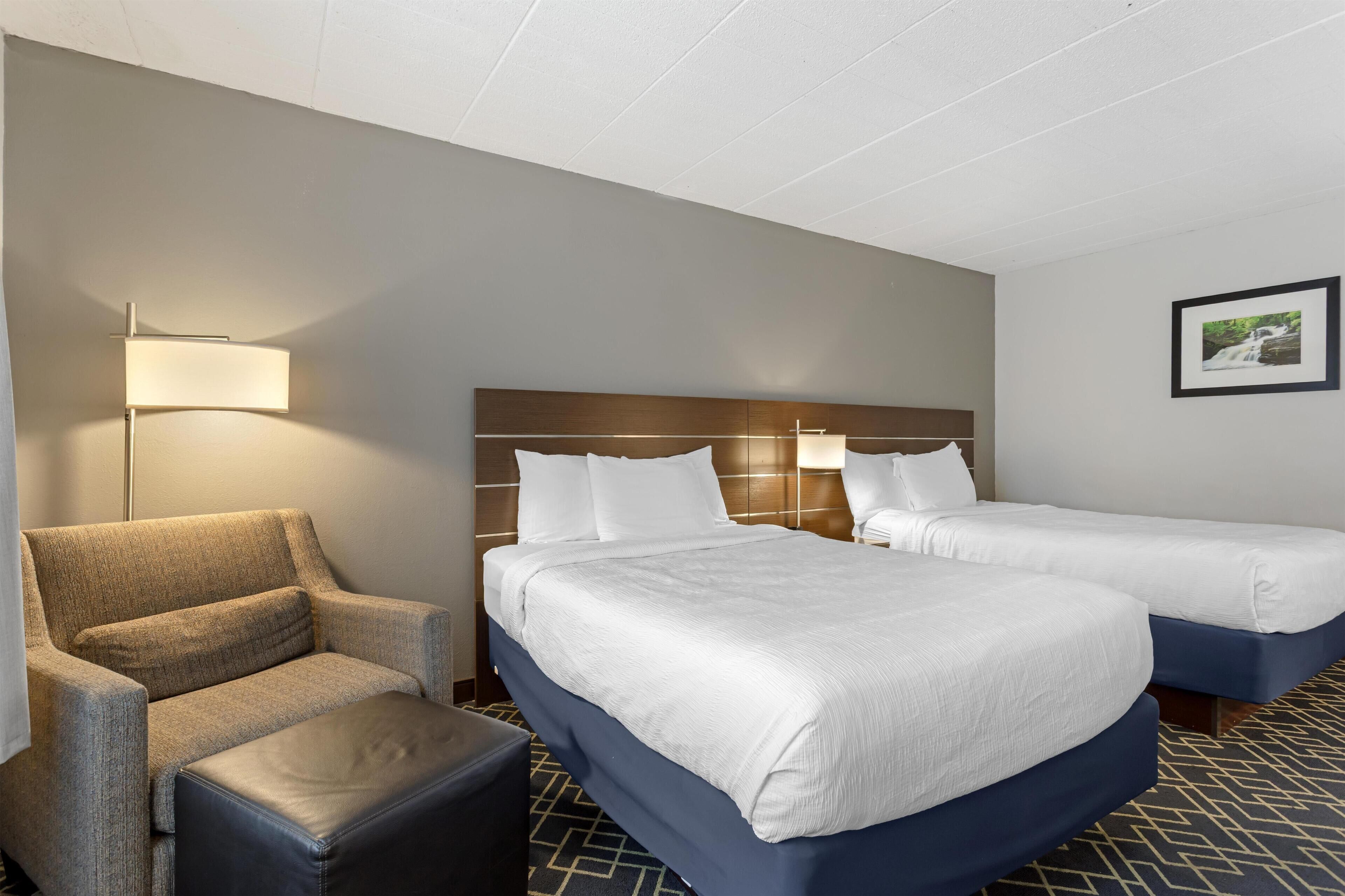 A hotel room with two beds, a sofa, a chair, and a lamp.