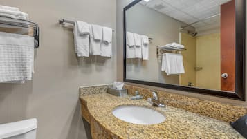 Un baño con lavamanos de encimera de granito, un espejo y varias toallas blancas colgadas en toalleros.